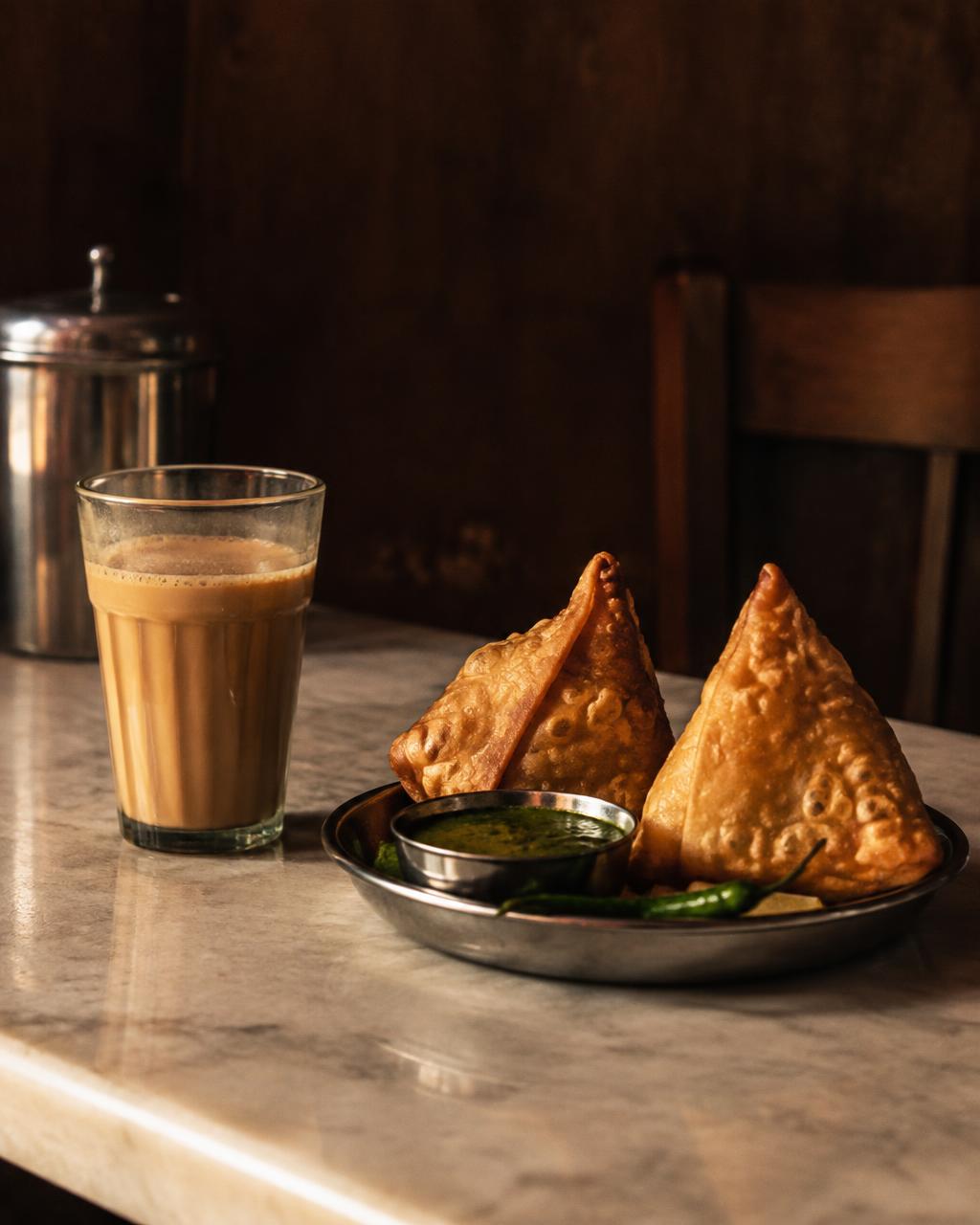 Samosas with green chutney beside a glass of chai